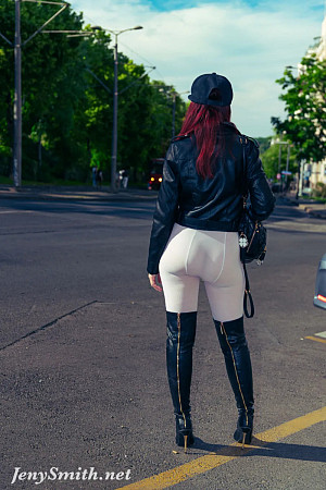 Exhibitionist Jeny Smith, wearing white tights, high leather boots and a black leather jacket, poses for a photoshoot on a crowded street.